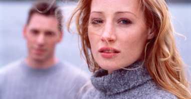 Young woman looking serious, young man in background. portrait