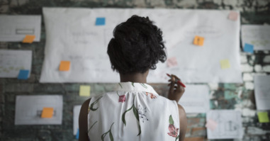 Creative businesswoman brainstorming, reviewing flow chart hanging on brick wall in office