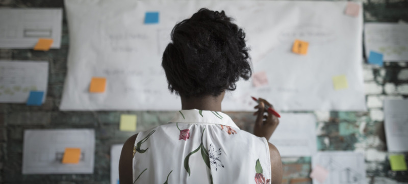 Creative businesswoman brainstorming, reviewing flow chart hanging on brick wall in office