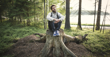 Thoughtful wonderlust man sitting on tree stump in forest