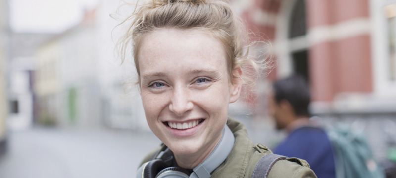 Portrait smiling young woman with headphones on city street