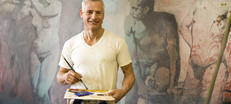 Mature artist with brush and pallette in front of painting, portrait