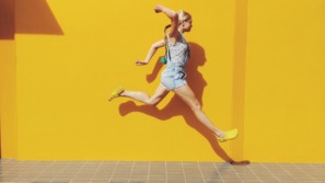 Side View Of Mid Adult Woman Jumping On Footpath Against Yellow Wall