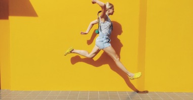 Side View Of Mid Adult Woman Jumping On Footpath Against Yellow Wall