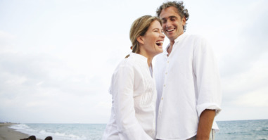 Couple standing on beach, smiling, children (7-9) in background
