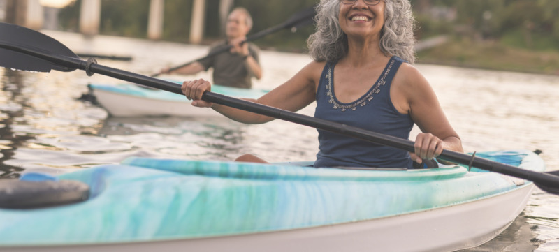 An ethnic senior woman smiles while kayaking with her husband