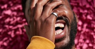 Close-up of young adult laughing while covering face against textured wall