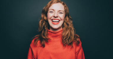 Portrait of woman in orange top laughing against gray background