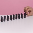 een hand die dominosteentjes omver duwt ter illustratie van de effecten van te veel stress