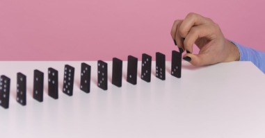 een hand die dominosteentjes omver duwt ter illustratie van de effecten van te veel stress
