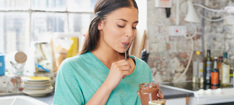 Pretty hispanic girl eating chocolate spread using spoon from jar