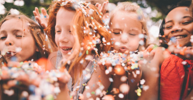 Colourful paper confetti being blown at the camera by children