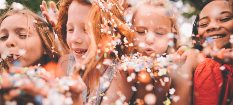 Colourful paper confetti being blown at the camera by children