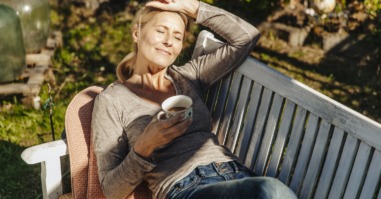 Woman with cup of coffee relaxing on garden bench