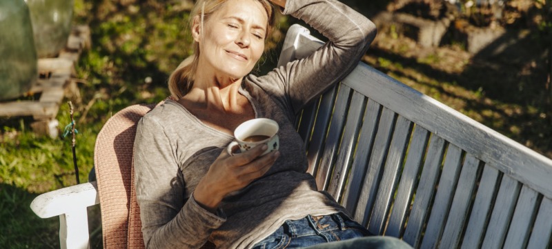 Woman with cup of coffee relaxing on garden bench