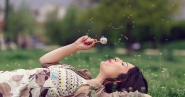Woman blowing dandelion in the park with copyspace