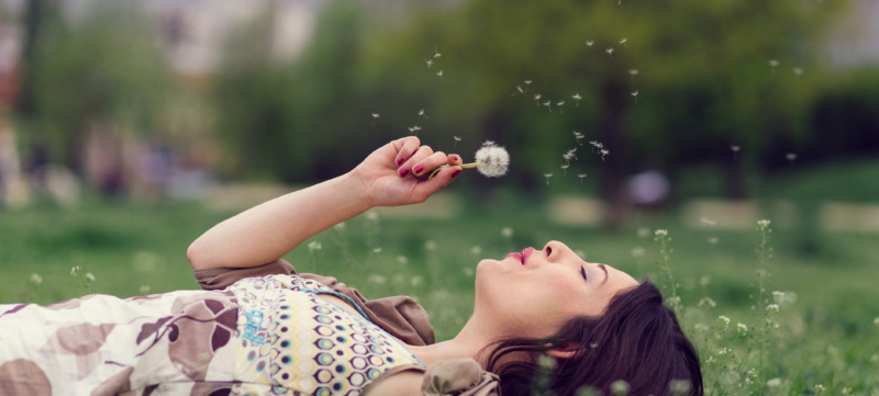 Woman blowing dandelion in the park with copyspace
