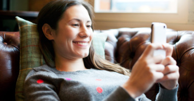 Woman lying on sofa using smartphone.
