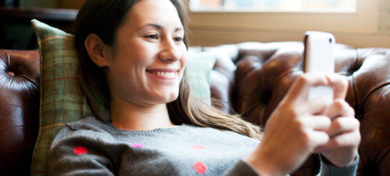 Woman lying on sofa using smartphone.
