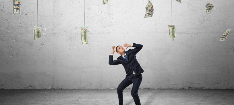 Scared businessman in protective pose with loads of money hanging