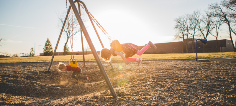 Little kids swinging on swing set on stomach