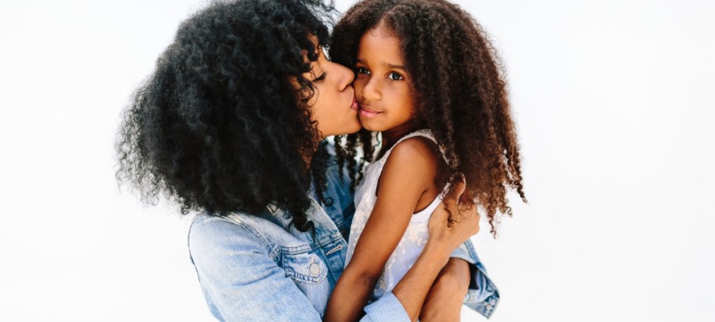 A Mother Giving Her Child A Kiss On The Cheek