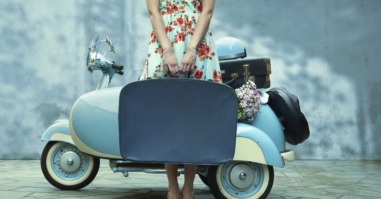 Pacific Islander woman holding suitcase near vintage scooter