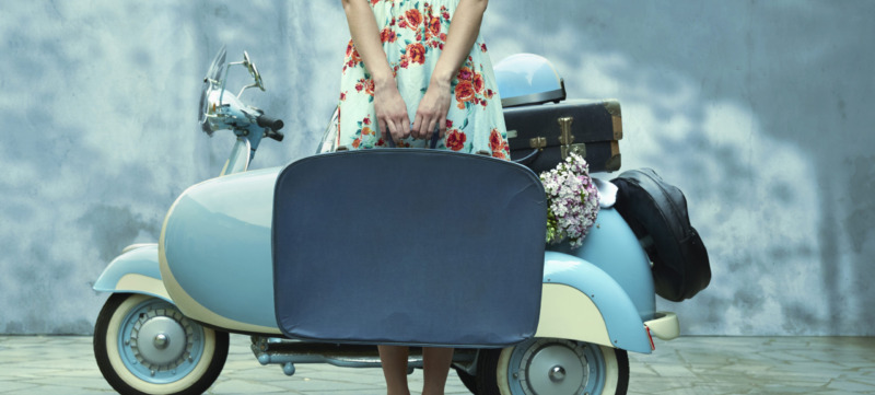 Pacific Islander woman holding suitcase near vintage scooter