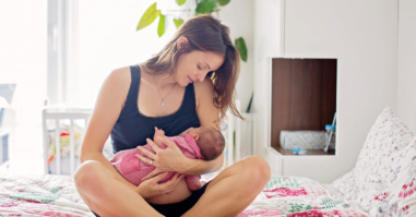 Young mother breastfeeds her baby, holding him in her arms and smiling from happiness