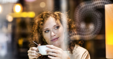 Portrait of smiling young woman with coffee cup behind windowpane of a coffee shop