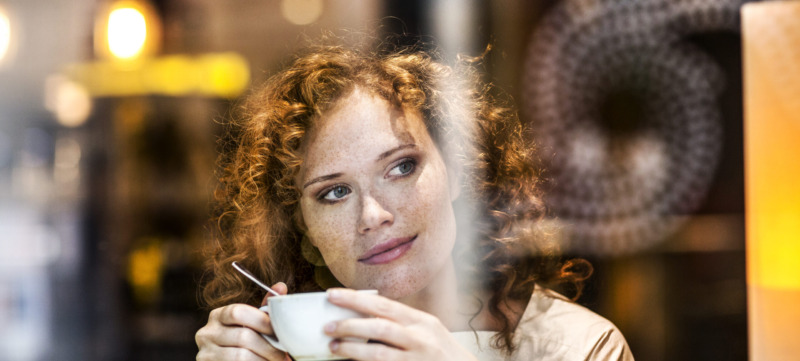 Portrait of smiling young woman with coffee cup behind windowpane of a coffee shop