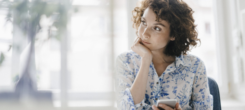 Businesswoman in office with smartphone and diary, looking worried