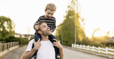 Happy father carrying son on shoulders while standing at street against clear sky
