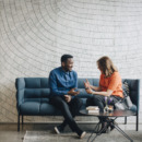 Businessman and woman taking while sitting on couch against wall at conference