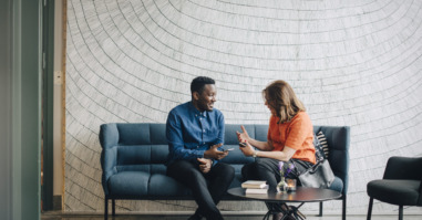 Businessman and woman taking while sitting on couch against wall at conference