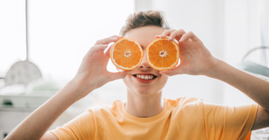 cheerful teenager male holding oranges in front of his eyes at kitchen in the morning