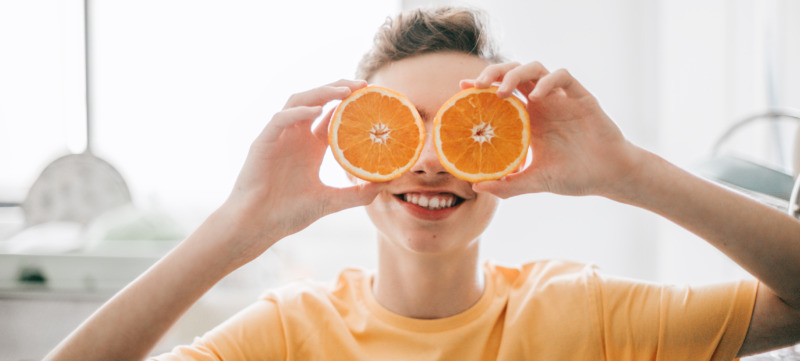 cheerful teenager male holding oranges in front of his eyes at kitchen in the morning