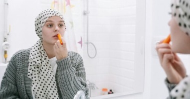 vrouw met doek om haar hoofd kijkt in de spiegel en doet lippenstift op