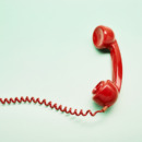 High angle view of a red old-fashioned telephone receiver with a coiled cable on turquoise background