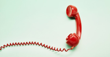 High angle view of a red old-fashioned telephone receiver with a coiled cable on turquoise background