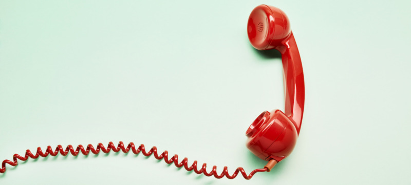 High angle view of a red old-fashioned telephone receiver with a coiled cable on turquoise background