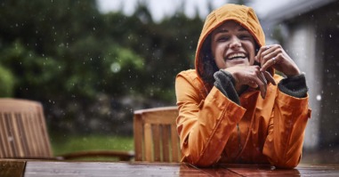 Portrait of happy woman wearing raincoat during heavy rain in garden