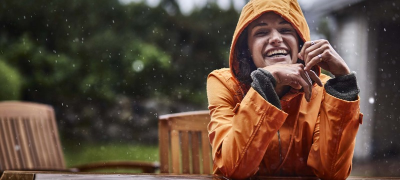 Portrait of happy woman wearing raincoat during heavy rain in garden