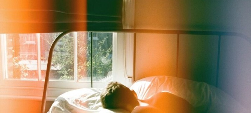 man ligt in een bed bij een raam en kijkt naar buiten