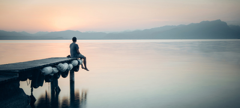 Italy, Lazise, man sitting on jetty looking at Lake Garda
