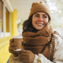 Smiling young woman looking away with disposable coffee cup at street cafe during winter