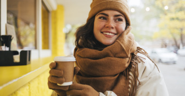 Smiling young woman looking away with disposable coffee cup at street cafe during winter