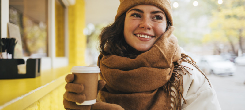 Smiling young woman looking away with disposable coffee cup at street cafe during winter