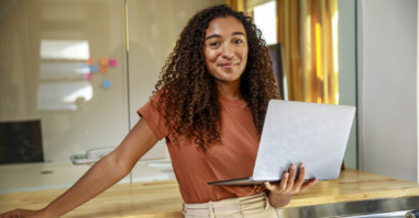 Smiling female entrepreneur with laptop standing in office