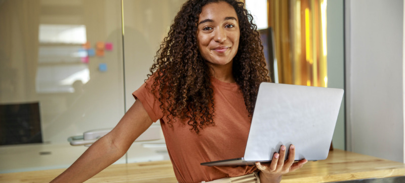 Smiling female entrepreneur with laptop standing in office
